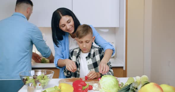 Mom Teaching Her 12-Aged Son to Cut Tomato while Her Husband Washing Lettuce for Joint Dinner