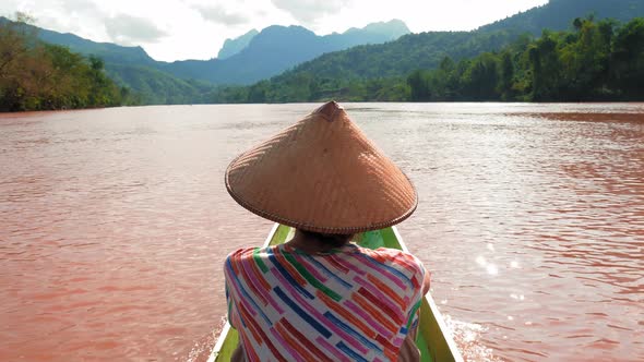 Woman with traditional hat cruising on the brown water of river in Laos