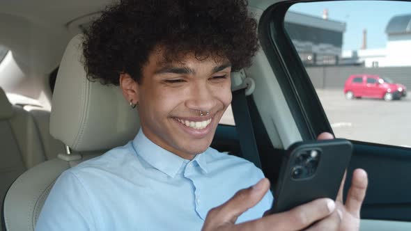 Young Business Guy of Ethnicity Scrolls the News Feed on the Smartphone While Sitting in the Car