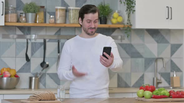 Young Man Doing Video Call on Smartphone While Standing in Kitchen