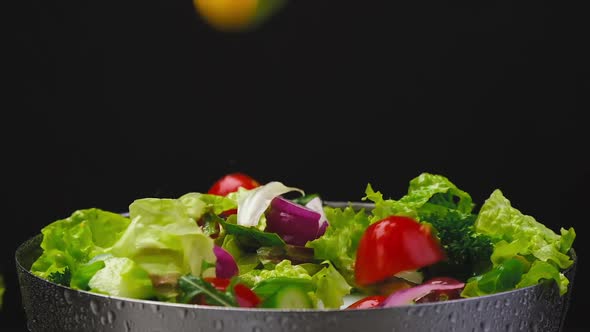 Fresh salad falling in bowl on black background