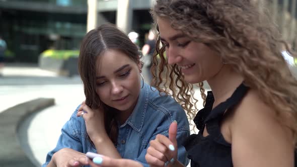 the Girlfriends Look at Something on Phone and Laugh. One Woman in Jeans and Ring Earrings, the