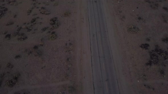 AERIAL: Birds View of Lonely Abandoned Desert Road with Red Car Driving in the Distance 