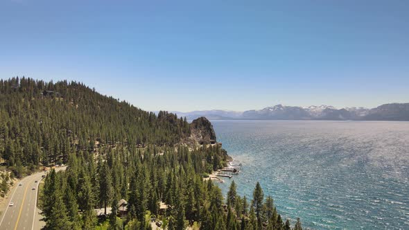 Drone flying towards cave rock with a thick forest and highway 50 on one side and Lake Tahoe and Des