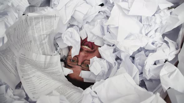 Man with Glasses Shouts From Under Pile of Crumpled Tax Papers Top View