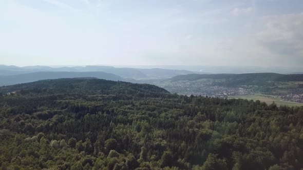 Drone flight over a forest in Switzerland. Far away are some villages visible.