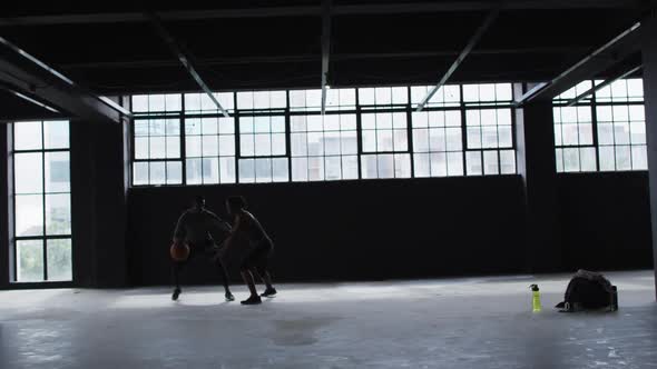 African american man and woman standing in an empty building playing basketball