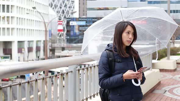 Woman texting message on mobile phone during raining