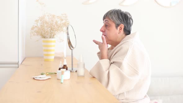 Elderly woman in bathrobe applying facial cream