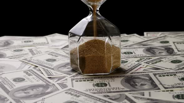 Hourglass with a pile of one hundred US banknotes