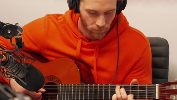 Pensive young man playing guitar into microphone while recording radio show