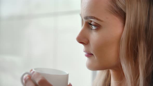 Cozy Winter Smiling Female Contemplating Out of Frozen Glass Drink Coffee Holding Mug Closeup