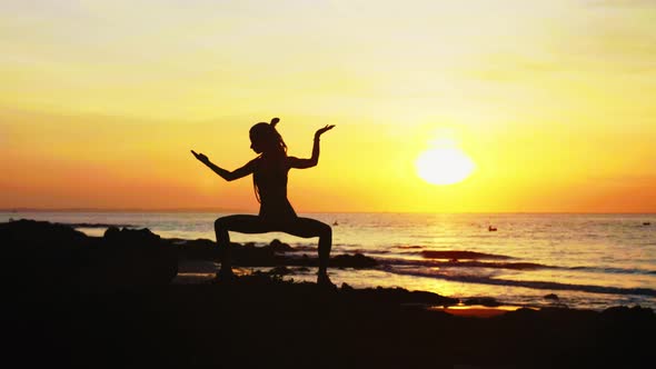 Young Woman's Silhouette Is Making Yoga Exercises on the Ocean Beach at Sunset.