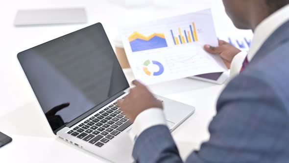 Rear View of African Businessman Working on Laptop and Reading Documents