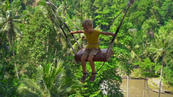 Slowmotion Shot of a Little Boy Swinging on Swings in a Tropical Surrounding. Travel To Bali Concept