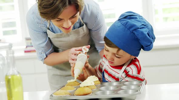 Mother helping boy to decorate cupcake with cream