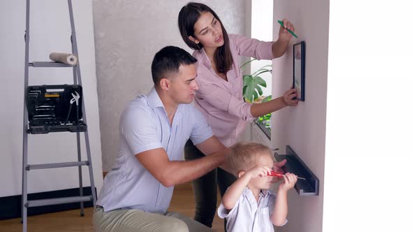 Friendly Family with Small Child Boy Doing Redecorating and Screwing Shelf and Picture To Wall