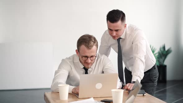 Two Young Successful Businessmen Work in the Office, Look at Laptop on the Table. Discuss Business