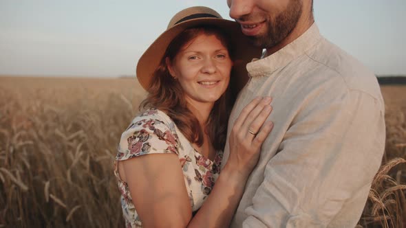 Happy Young Family Couple Hugs in a Wheat Field and Smiling Look at Each Other and Kiss