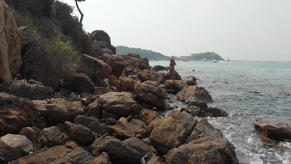 Lady with Dark Hair Stands on Huge Stone Against Blue Sea