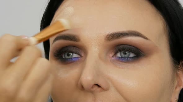 Close Up View of a Stylist Makeup Artist Applies Foundation Cream with a Special Brush on the Face