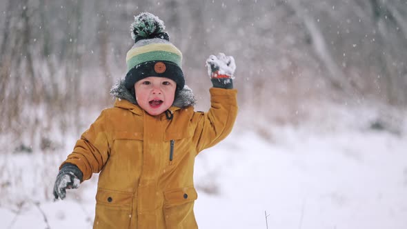 Happy Toddler Boy Having Fun and Playing Snowballs on Winter Snowfall Background