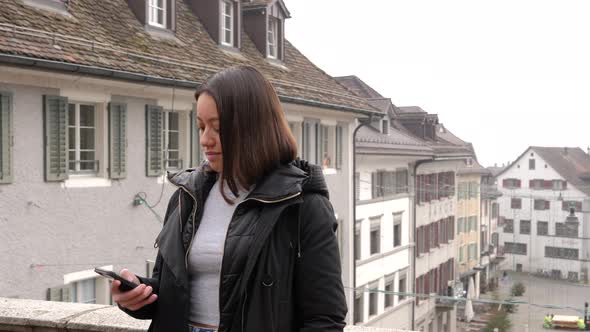 Young attractive woman standing in front of city of Rapperswil, Switzerland. Typing on smartphone. S