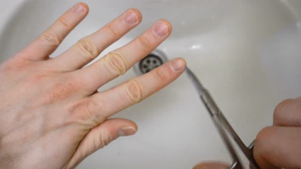 Male Nail Grooming with Scissors on Finger Over Sink or Wash Basin in the Morning