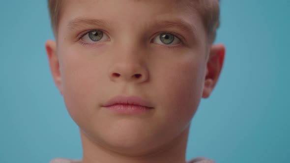 Portrait of serious boy looking at camera and then smiling on blue background