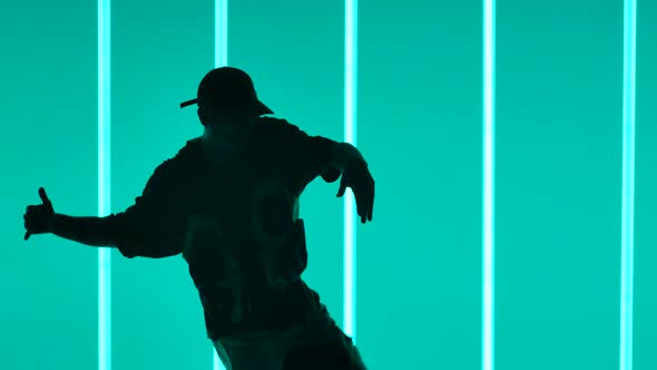 An Active Hipster Young Man Dancing in a Dark Studio Illuminated By Neon Lights