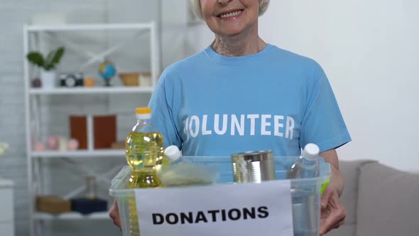 Elderly Lady Volunteer Holding Box With Food, Looking to Camera and Smiling, Aid