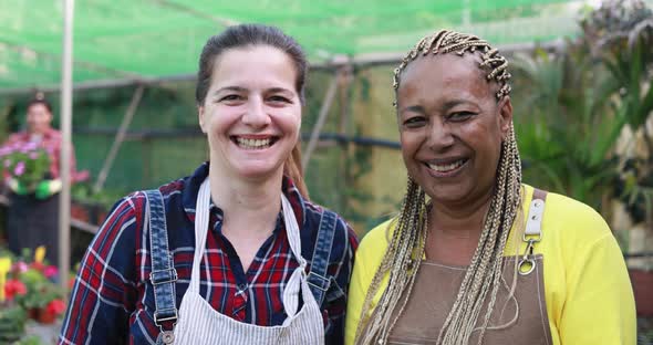 Multiracial senior women working inside greenhouse garden while smiling on camera