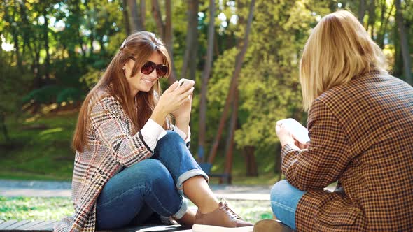 Happy girls browsing photos in social media sitting in green park