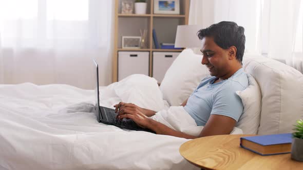 Happy Indian Man with Laptop in Bed at Home