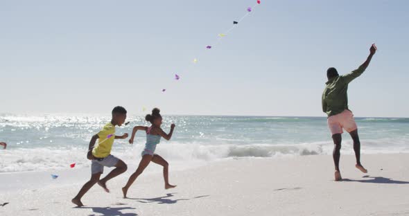 Smiling african american family running and flying kite on sunny beach