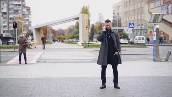 Portrait of a man having a phone talk outdoors. Handsome businessman in suit and warm coat