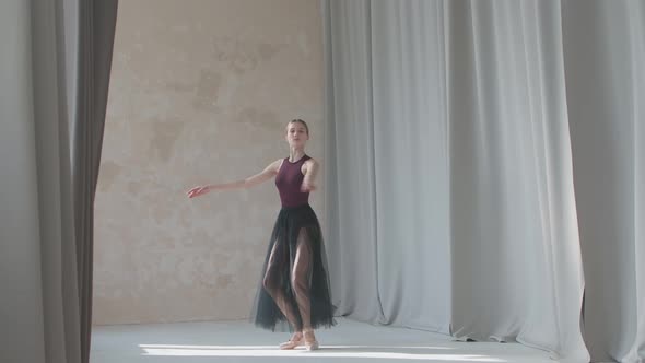 Young Graceful Ballerina Against the Background of Long Light Curtains Performs a Pirouette Movement