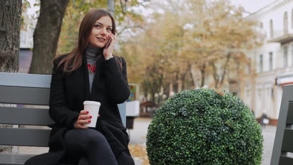 Business Woman Talking on the Phone and Drink Coffee on the Bench in the Street