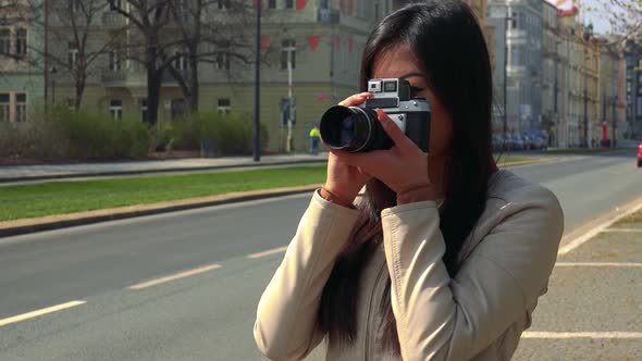 A Young Asian Woman Takes Pictures with a Camera in a Street in an Urban Area