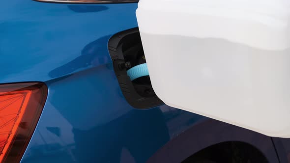 Close Up Man Filling a Diesel Engine Fluid From Canister Into the Tank of a Blue Car