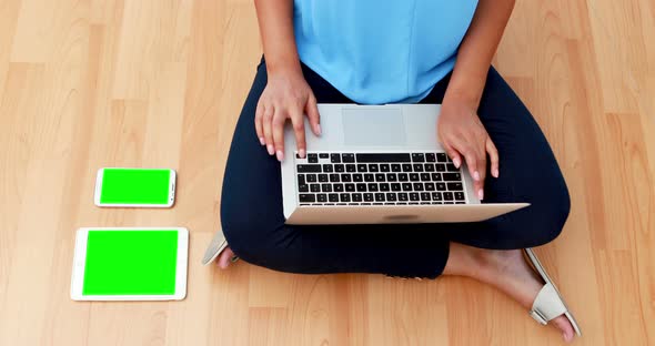 Female executive using laptop while sitting on wooden floor 4k