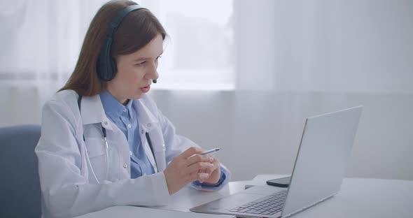 Female Family Doctor Is Consulting Online, Talking with Patient By Video Chat at Laptop, Working
