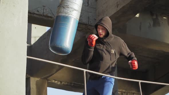 A boxer in red gloves trains blows on a punching bag in an abandoned building. Outdoor workout