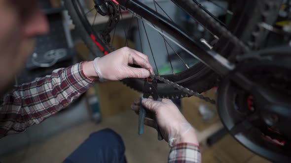 Male Mechanic Working in Bicycle Repair Shop Worker Repairing Bike Chain Using Special Instrument