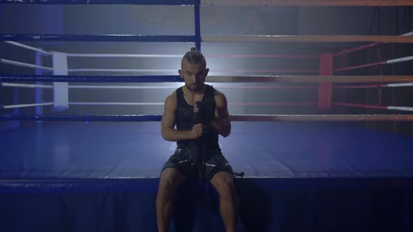 Muscular Wrestler Reel Up Black Bandages for Boxing Before Fight Sitting Near Ring