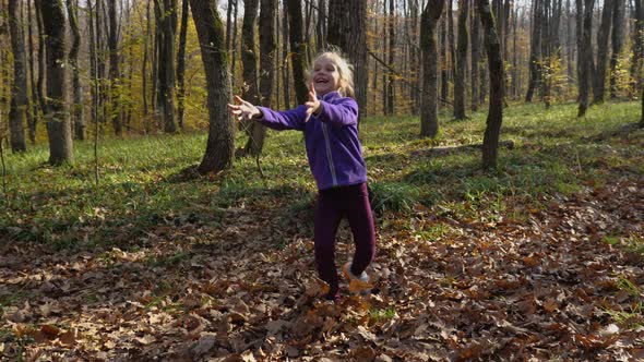 A joyful blond child playing ball in the autumn forest