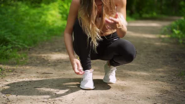 A Woman Ties Her Shoelaces While Running Through the Woods