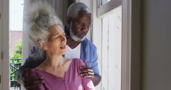 Mixed race senior couple talking to each other while looking out of the window at home