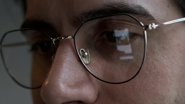 Close-Up Of a man with Glasses Watching news on a Smartphone, Reflection on Lenses, Dark Room