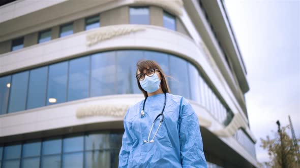 Sad Female Doctor in Glasses and Medical Face Mask Looking Away Near Hospital